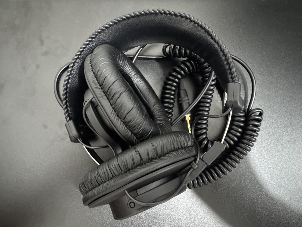 「折りたたんで収納されたSONY MDR-7506モニターヘッドホン。カールコードと3.5mmプラグが見える」
